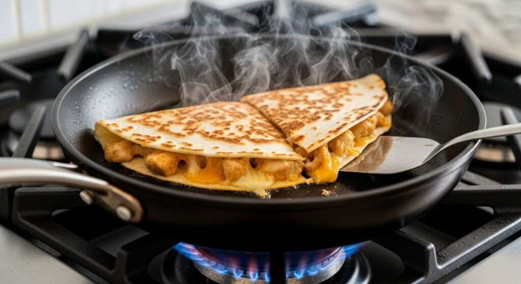 A chicken quesadilla sizzling and browning in a hot non-stick skillet.